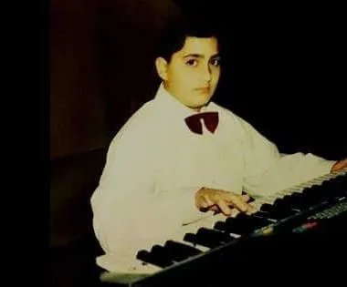 Majed as a boy in a white shirt and bow tie, playing a keyboard