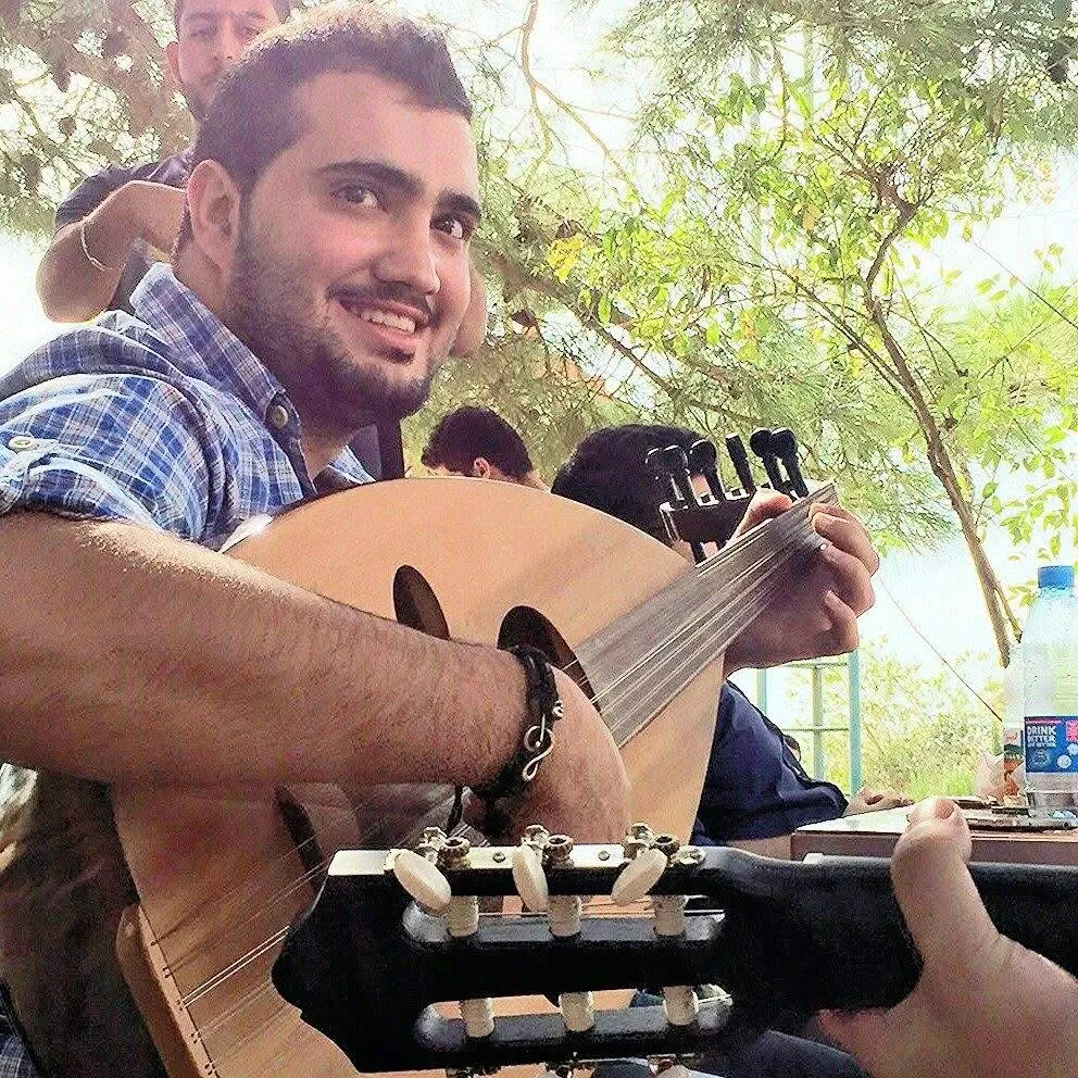 A younger Majed playing the oud outdoors among friends