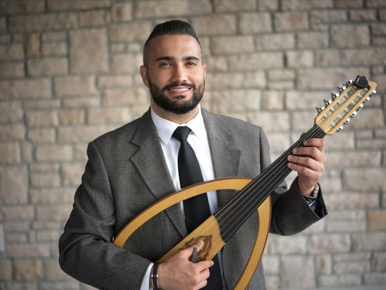Majed with his oud against a stone wall